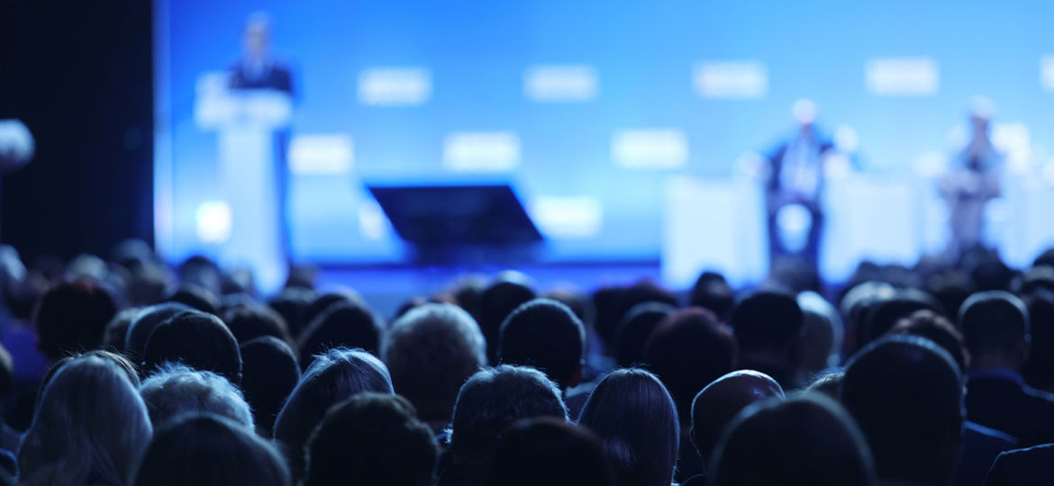 Business and entrepreneurship symposium. Speaker giving a talk at business meeting. Audience in the conference hall. Rear view of unrecognized participant in audience.